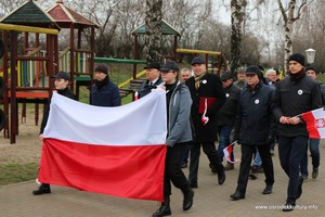 Zdjęcie przedstawia maszerujących ludzi z dużą flagą Polski. (photo)