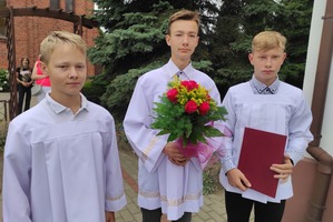 Na zdjęciu znajduje się trzech ministrantów jeden z nich trzyma bukiet kwiatów. (photo)