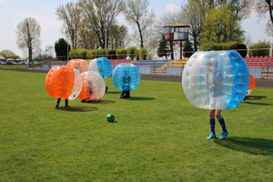 Dzieci w dmuchanych kulach, grające w piłkę nożną na boisku. (photo)