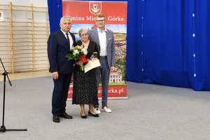 Na zdjęciu znajduje się dwóch mężczyzn oraz kobieta trzymająca bukiet kwiatów. (photo)