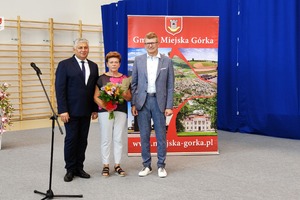 Na zdjęciu znajduje się dwóch mężczyzn oraz kobieta trzymająca bukiet kwiatów. (photo)