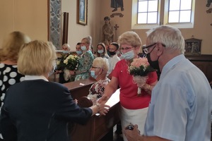 Na zdjęciu znajduje się grupa ludzi, w której składzie dwie kobiety przekazują sobie kwiaty. (photo)