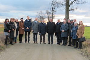 Na zdjęciu stoją uczestnicy spotkania z wicemarszałkiem województwa wielkopolskiego. Delegacja stoi na dworze, na wykonanej drodze. (photo)